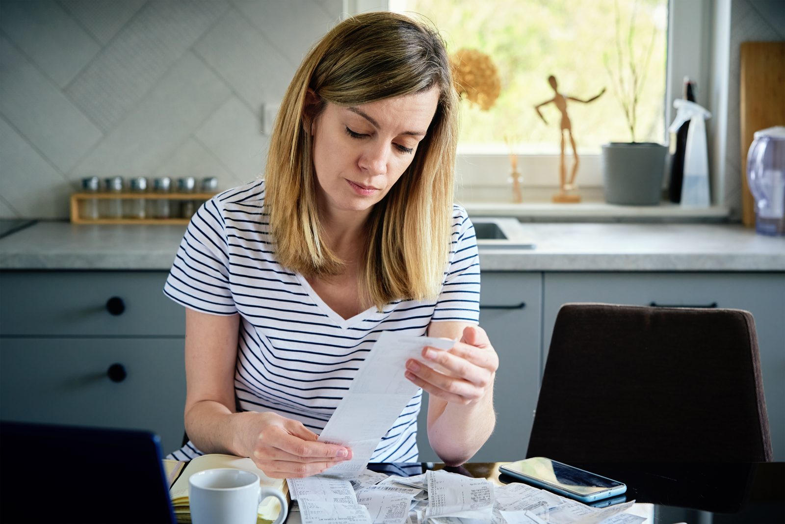 Woman reviewing bills and a charged-off account notice at her kitchen table